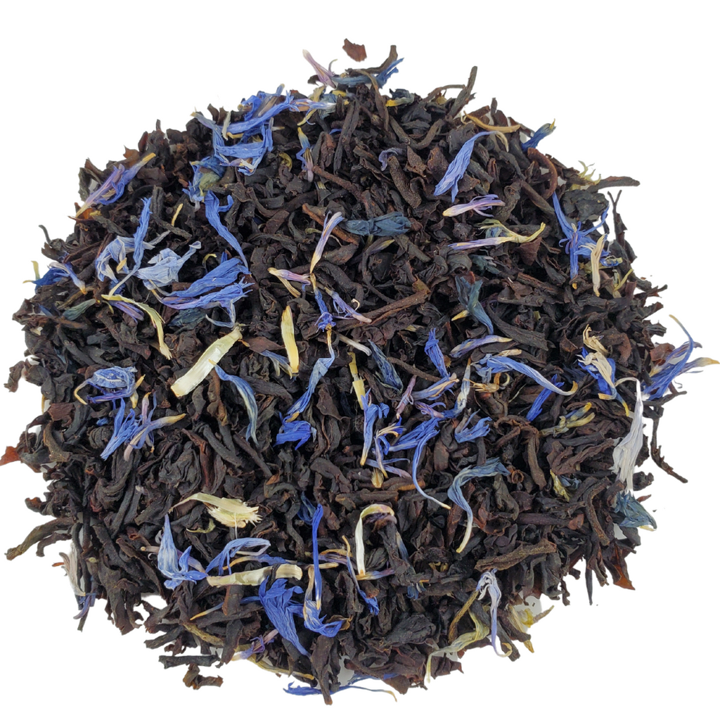 Dry black tea leaves with blue and yellow flowers on a white background