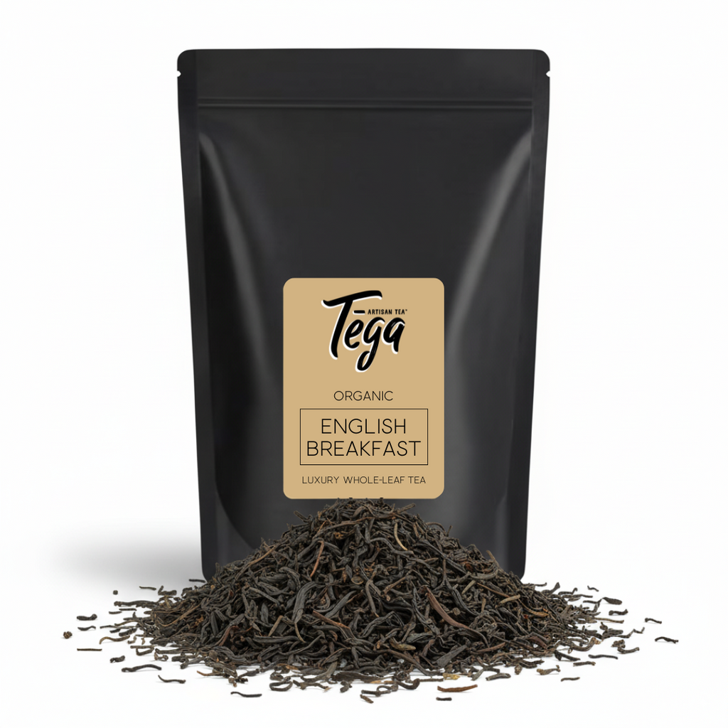 Black tea packaging with Tega label and loose tea leaves on a white background