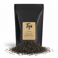 Black tea packaging with Tega label and loose tea leaves on a white background
