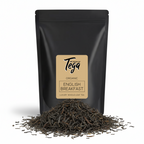 Black tea packaging with Tega label and loose tea leaves on a white background