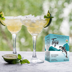 Two glasses of iced tea with lime wedges and a box of Tega Ice Wine on a table outdoors.