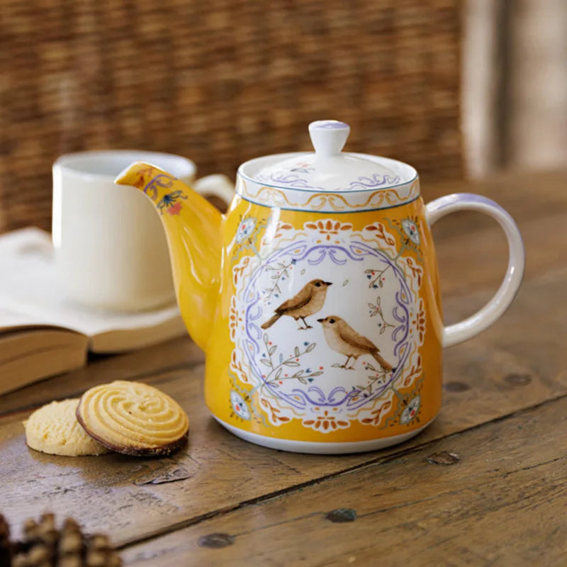 Yellow teapot with bird design on a wooden table with cookies and a book.