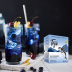 Two glasses of blue berry tea with ice and cherries, next to a box of Tega Blueberry with Lavender tea.