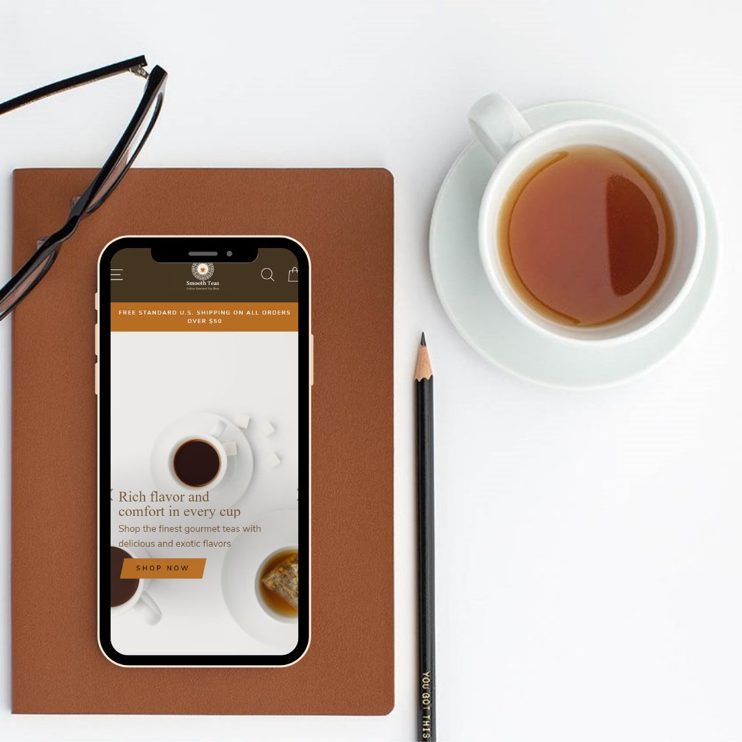 Smartphone displaying a tea advertisement on a brown notebook with a cup of tea, pencil, and glasses on a white surface.