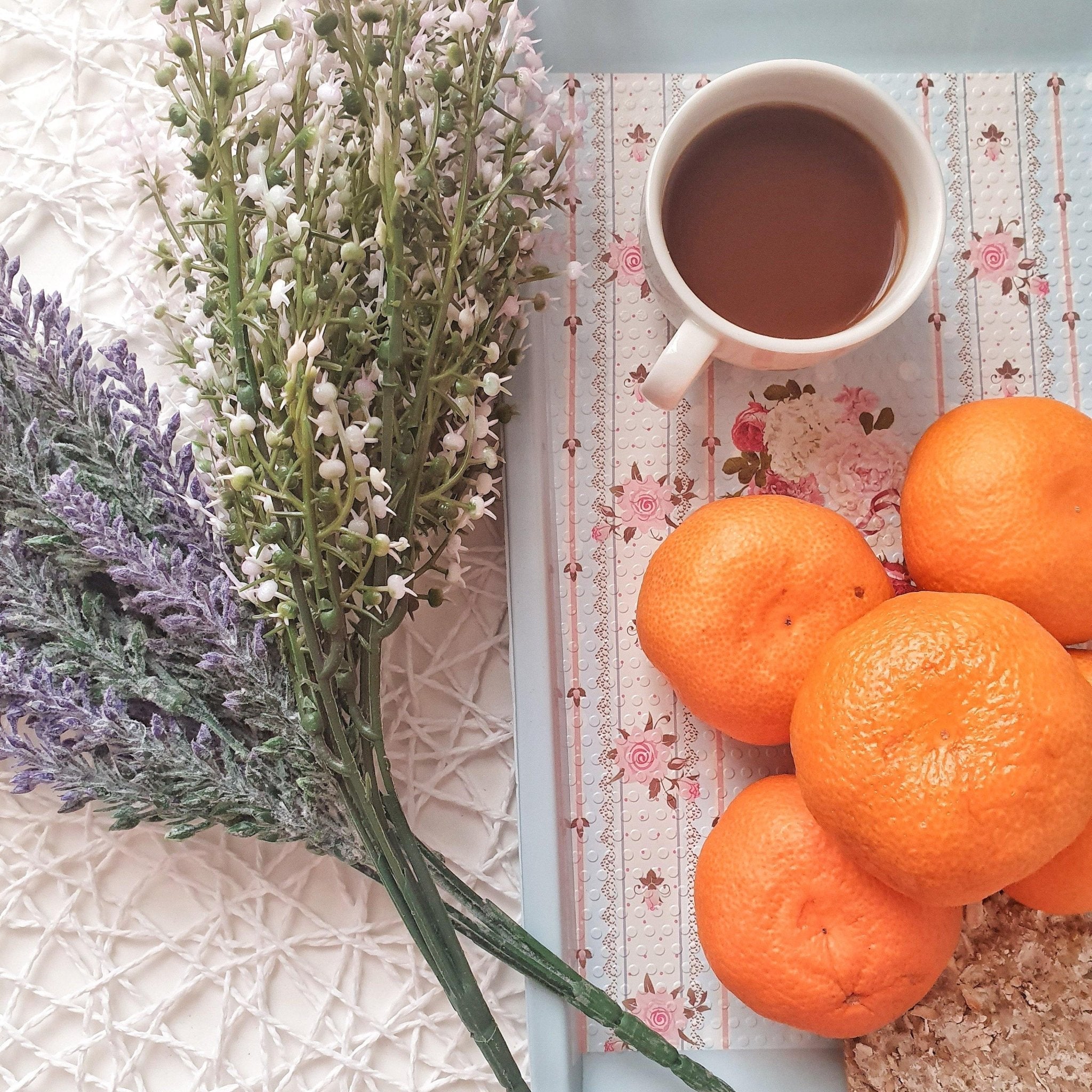 Oranges, a cup of tea, and flowers on a textured surface with floral pattern
