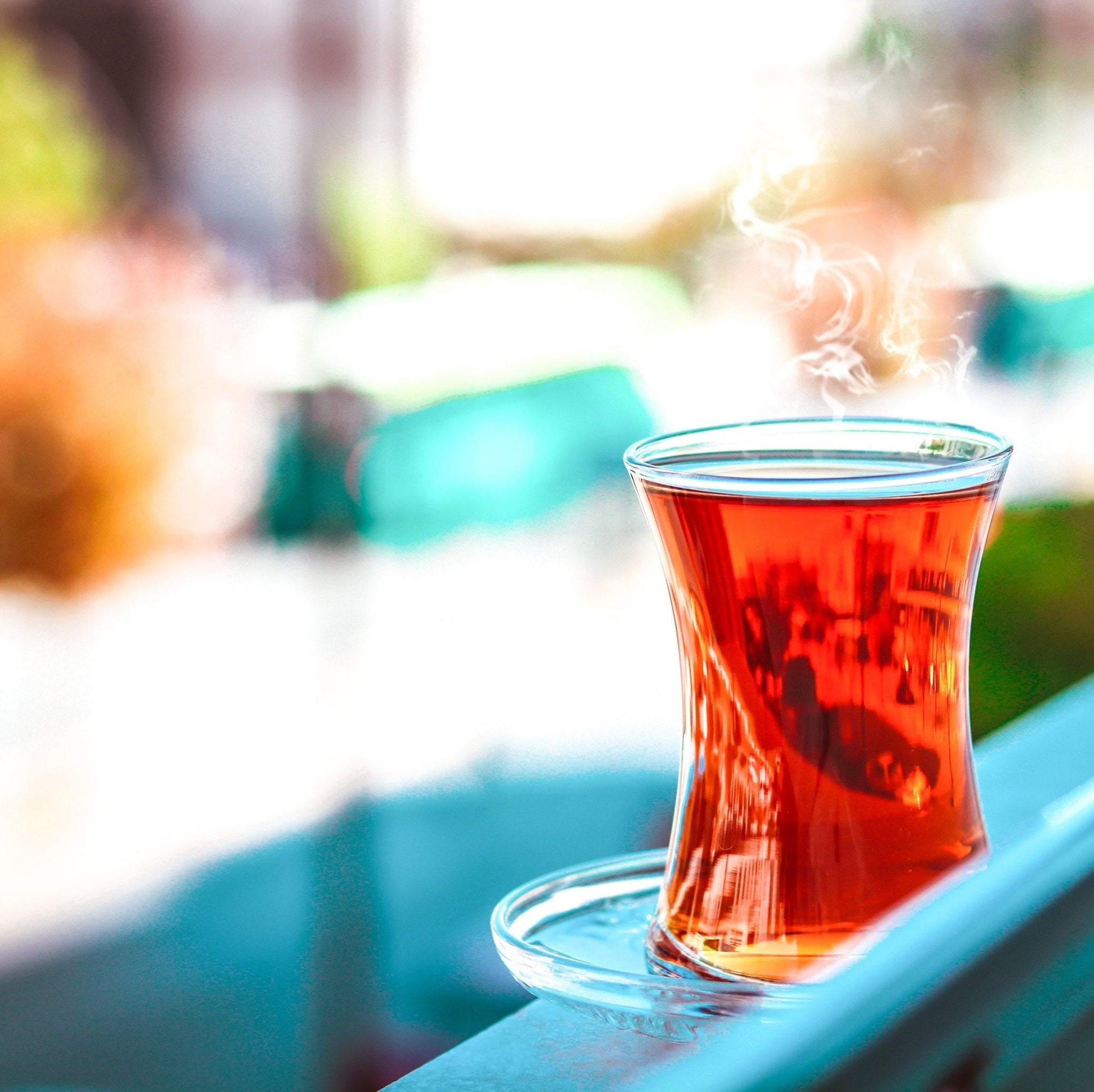 Steaming glass of red tea on a blue surface with a blurred outdoor background