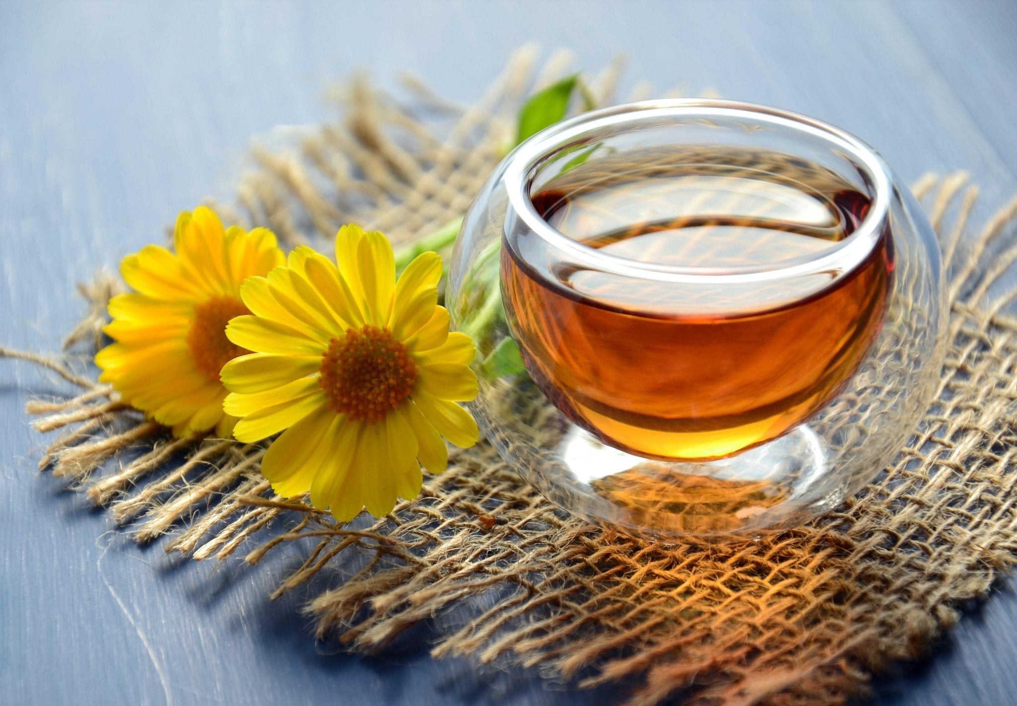Glass of amber liquid with yellow flowers on a textured surface