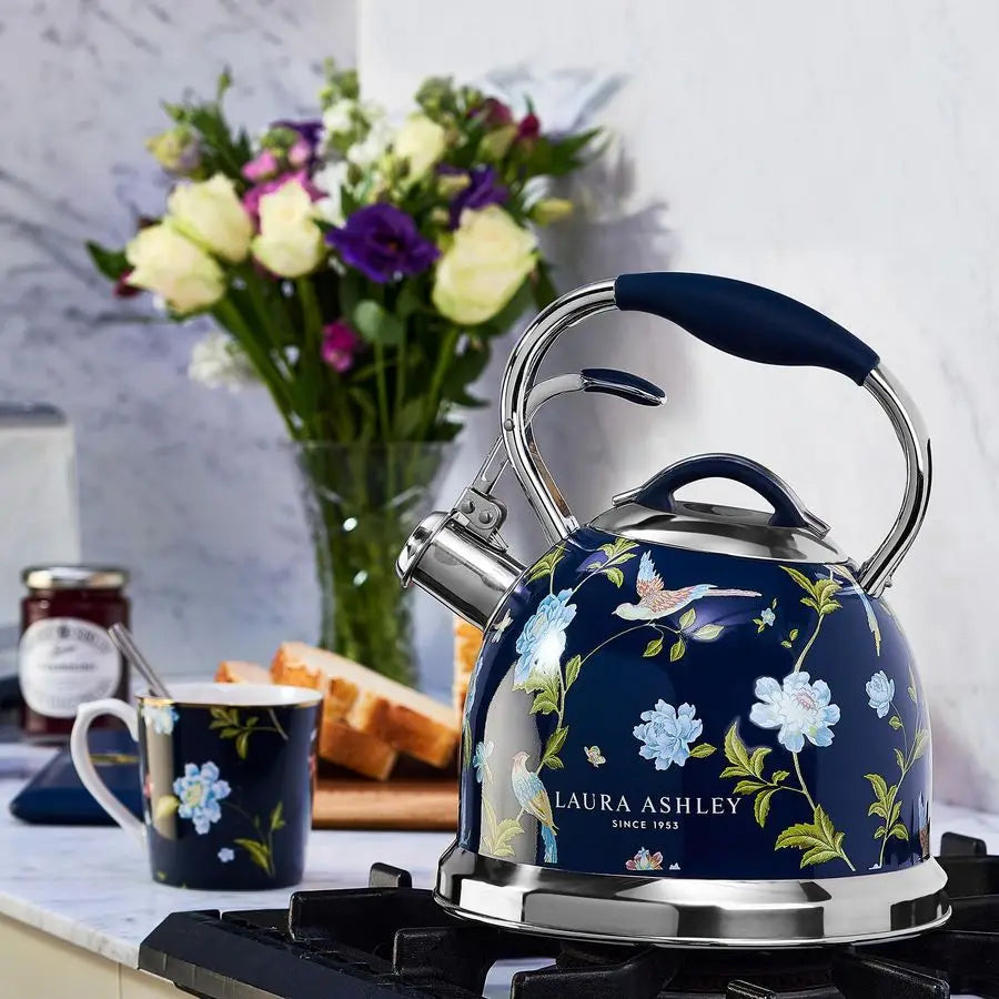 Floral-patterned kettle on a stove with a cup and flowers in the background