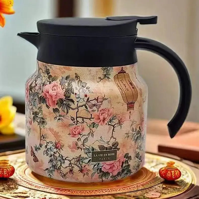 Floral-patterned teapot with black lid and handle on a decorative surface.