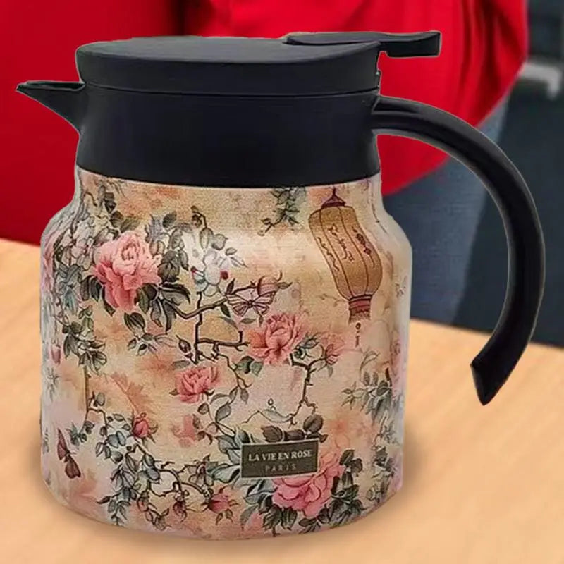 Floral-patterned thermos with black lid and handle on a wooden surface.