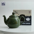 Green teapot on a white surface with a box in the background, featuring 'London Pottery' branding.
