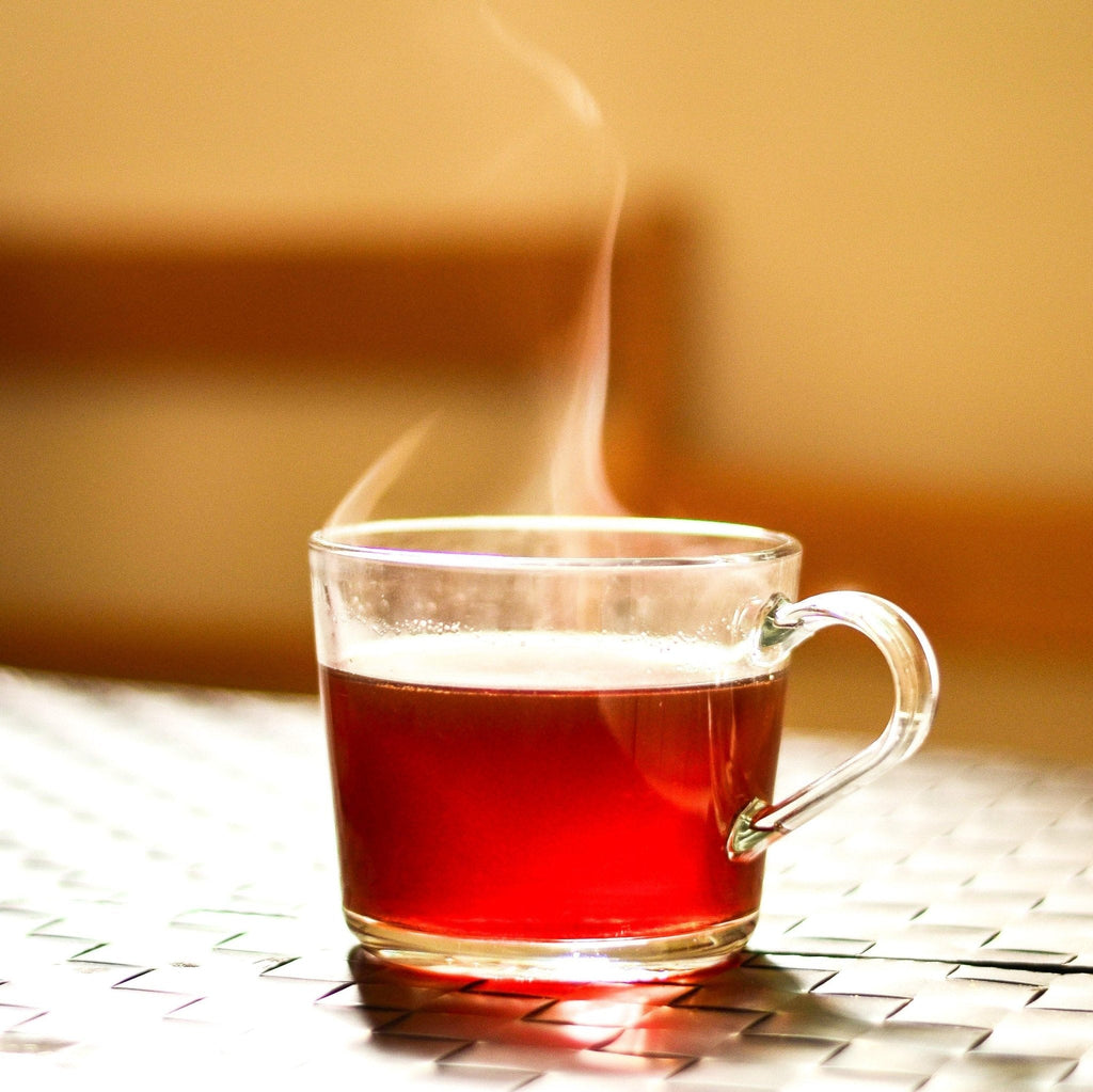 Steaming glass mug of hot liquid on a textured surface with a blurred background