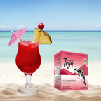 Red cocktail with pineapple and cherry on a beach, next to a box of Tega Cranberry with Ginger tea.